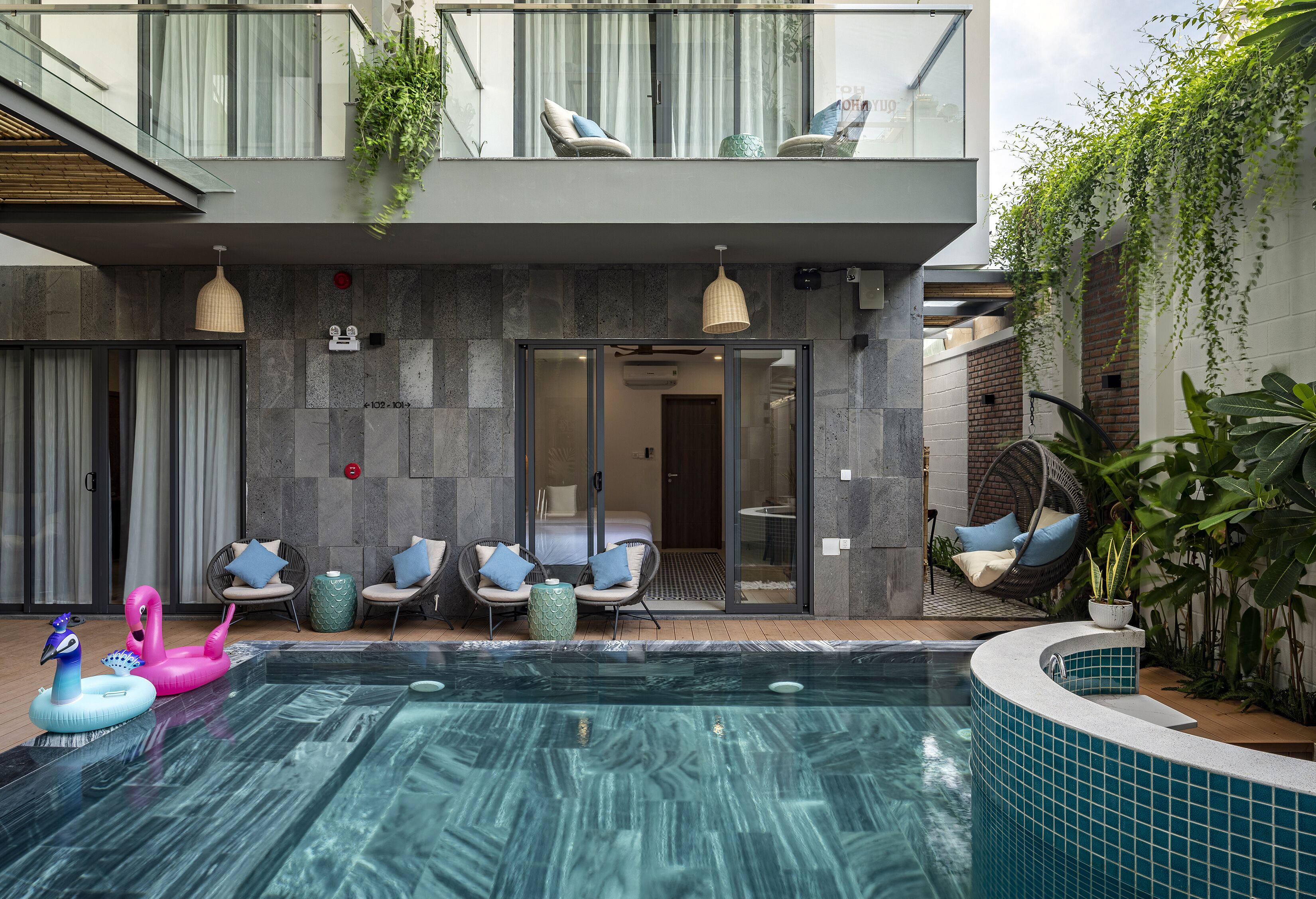Un hotel moderno con zona de piscina, mobiliario exterior y balcón con plantas.