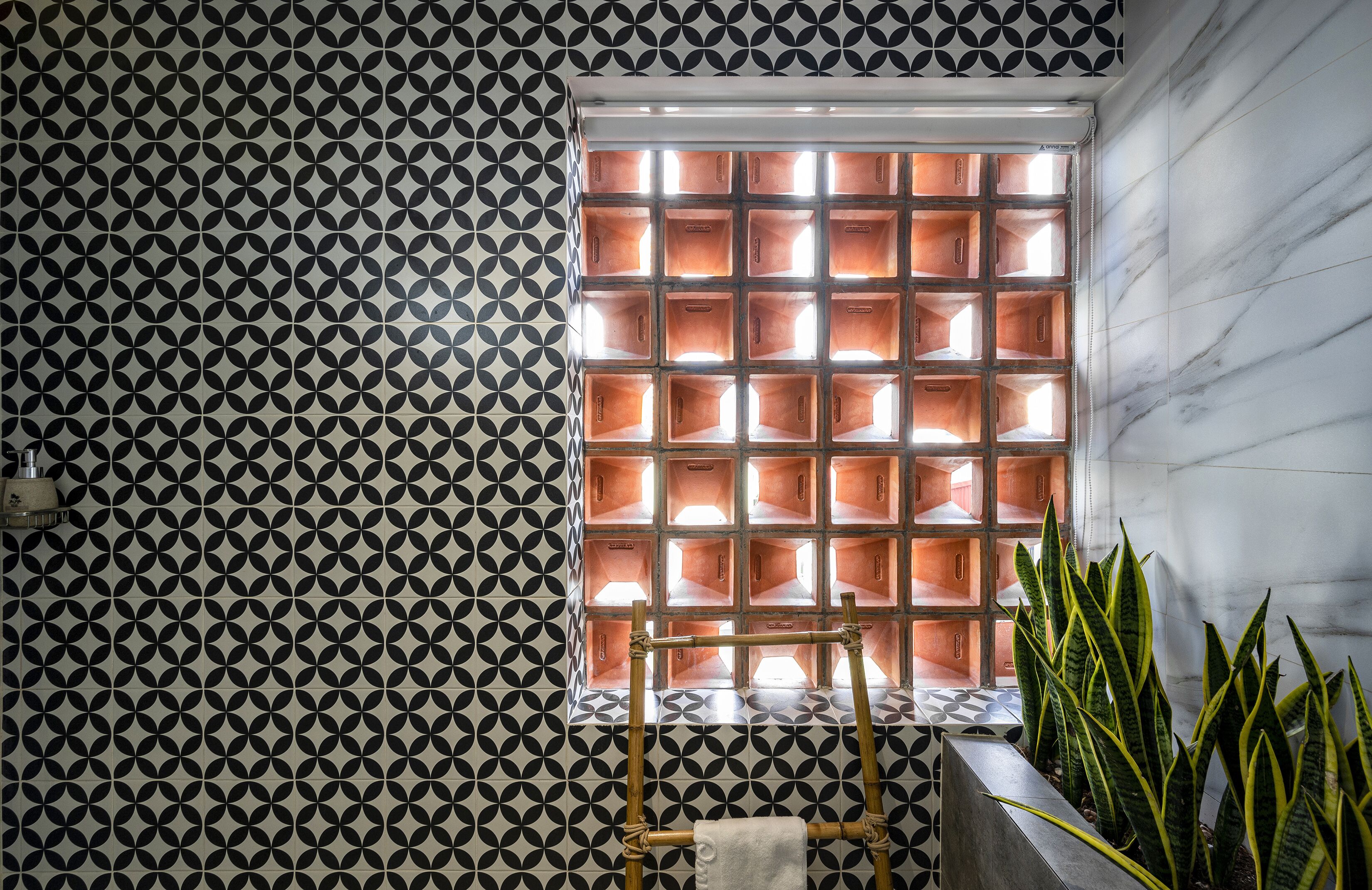 Ein Badezimmer mit Wand in geometrischem Muster, einem Fenster mit mehreren Fächern und einer Pflanze in der Ecke.