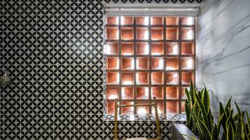 A bathroom with a geometric patterned wall, a window with multiple compartments, and a plant in the corner.