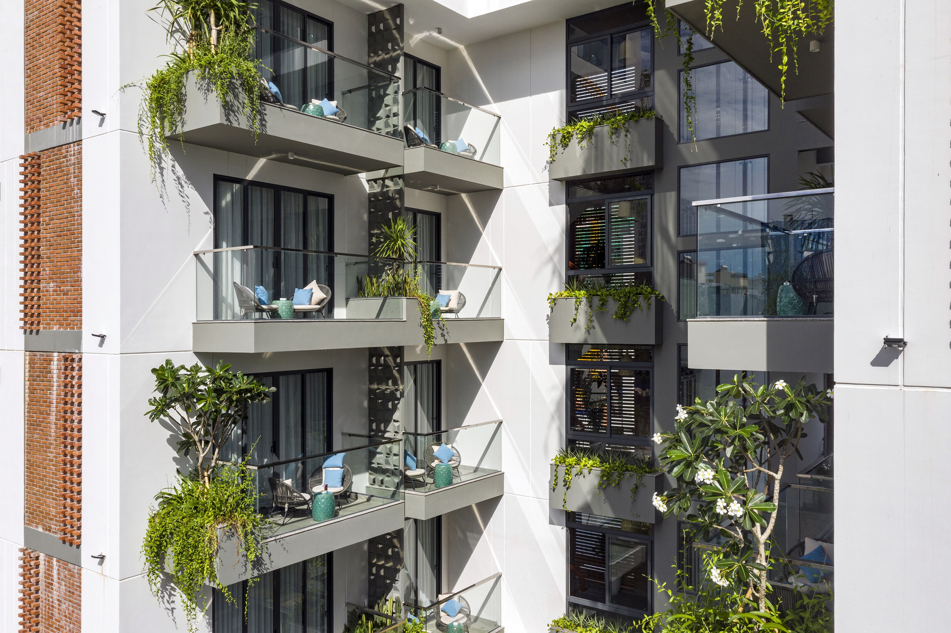 A modern multi-story building with balconies, some with plants and outdoor seating.