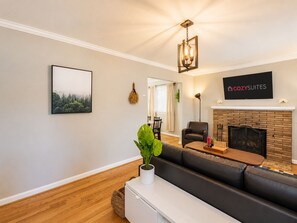 A modern living room with a fireplace, a sofa, a dining area, and a mounted TV. - Gorgeous Home 10 min to DC by CozySuites (Alexandria)