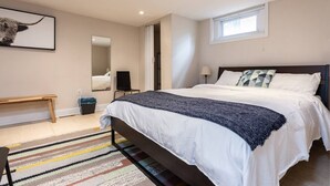 A modern bedroom with a large bed, a bench, a mirror, and a window.