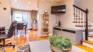 A modern living room with a dining area, a staircase, and a kitchen in the background.