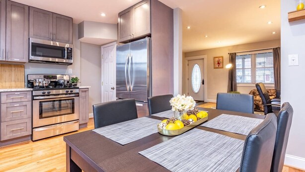 A modern kitchen with stainless steel appliances, a dining area with a table set for two, and a living area with a sofa and a window.