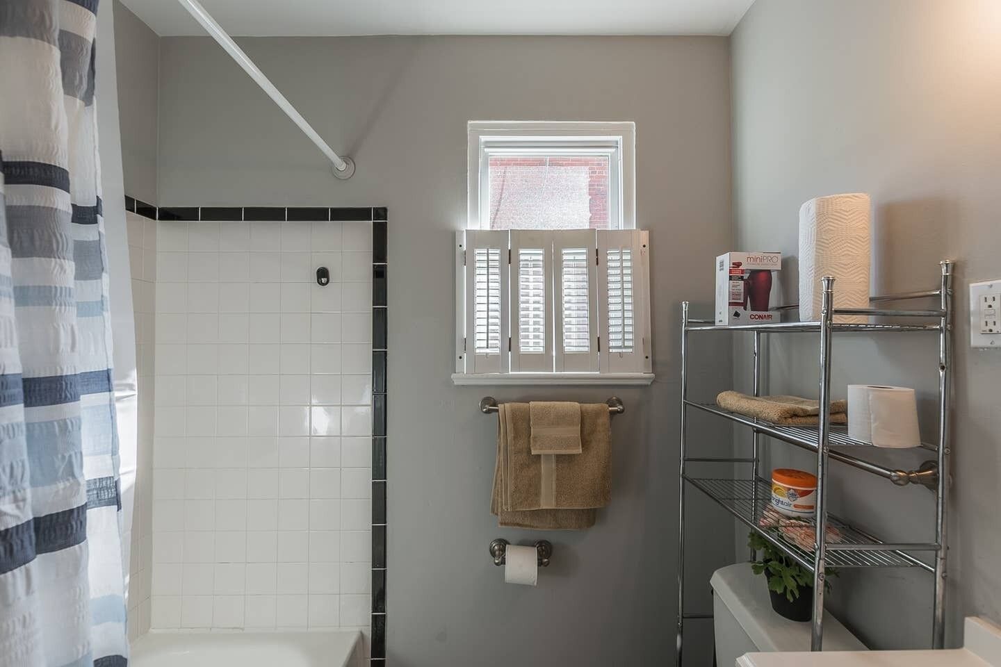 A bathroom with a shower, a window, a towel rack, and a shelf with toiletries.