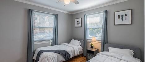 Ein Schlafzimmer mit zwei Betten, einem Deckenventilator, einem Nachttisch mit Lampe und gerahmten Bildern an der Wand.