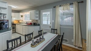 A compact kitchen with white cabinets, a dining table set for four, and a window with blinds. - Enchanting historic townhouse by CozySuites (Alexandria)
