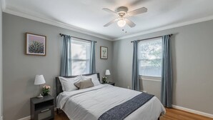 A bedroom with a bed, bedside tables, a ceiling fan, and two windows with curtains. - Enchanting historic townhouse by CozySuites (Alexandria)