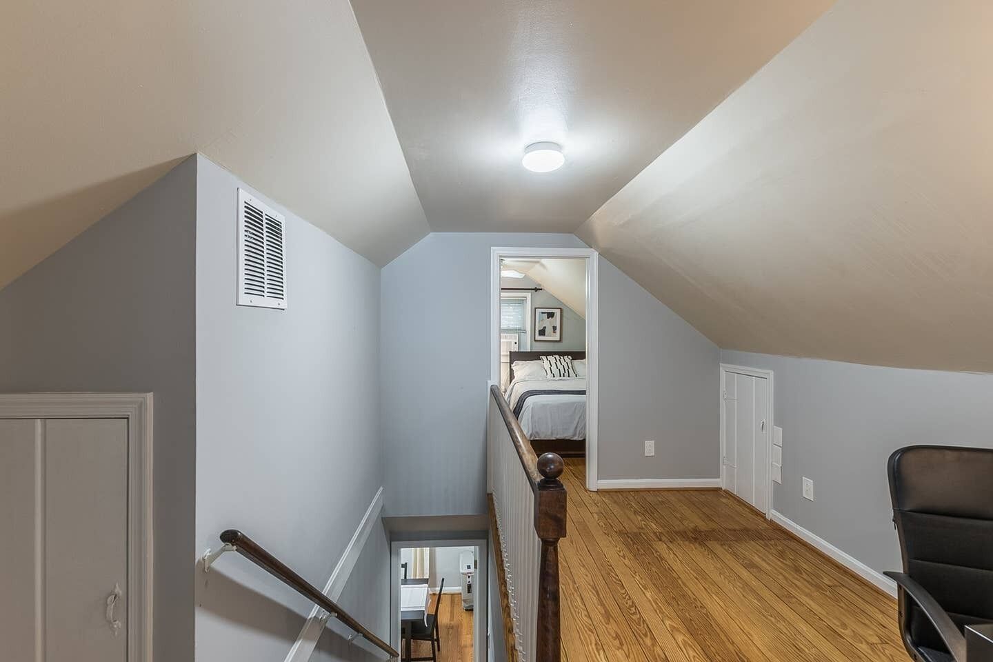 A spacious attic bedroom with a wooden floor, a bed, and a staircase leading to a bathroom.