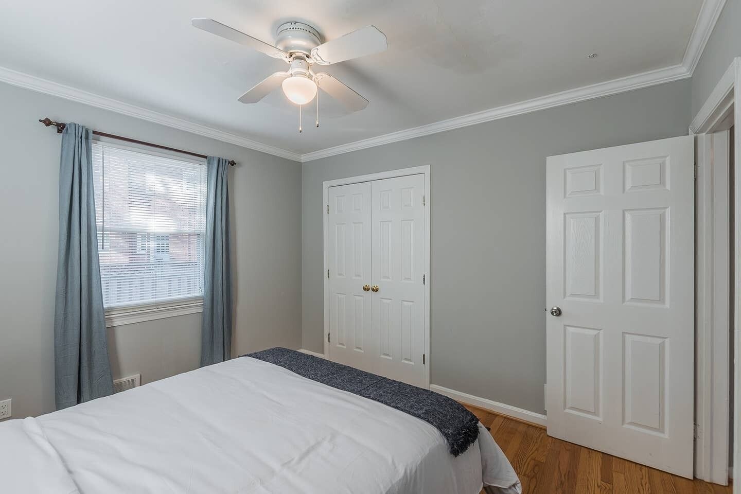 A bedroom with a bed, a ceiling fan, two white doors, and a window with curtains.