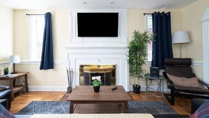 A living room with a fireplace, a television mounted above it, a sofa, a coffee table, and a chair. - Spacious 4BR CozySuites in Old Town Alexandria (Alexandria)