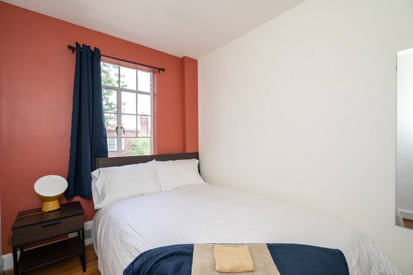 Een slaapkamer met een bed, nachtkastje, lamp en raam met gordijnen.
