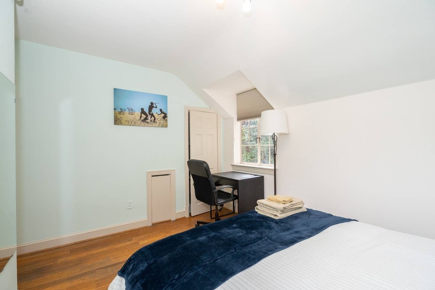 A bedroom with a bed, a desk, a chair, a lamp, a window, and a door.