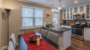 A modern kitchen with white cabinets, a granite countertop, stainless steel appliances, and a dining area with a red placemat.