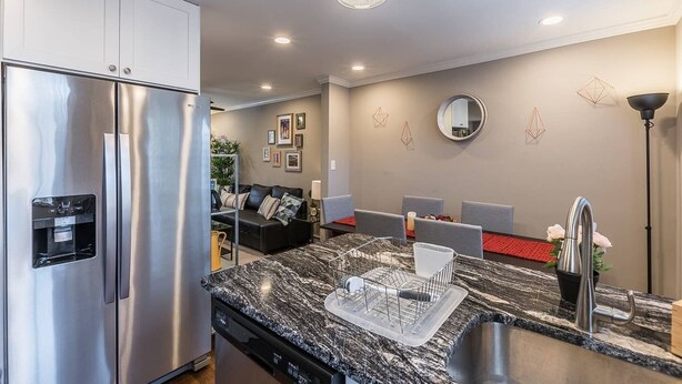 A modern kitchen with a stainless steel refrigerator, a granite countertop, and a built-in dishwasher.