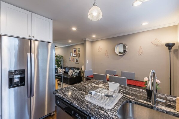 A modern kitchen with a stainless steel refrigerator, a granite countertop, and a built-in dishwasher. - Beautiful 3br/2ba House with cozy backyard by CozySuites (Alexandria)