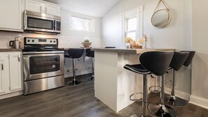 A modern kitchen with stainless steel appliances, white cabinetry, and a bar area with black stools. - Louisville Dream House 4BR/2BA  by CozySuites (Louisville)