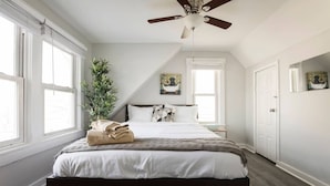 A bedroom with a bed, a ceiling fan, a window, a plant, and a door. - Louisville Dream House 4BR/2BA  by CozySuites (Louisville)