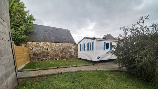 Een wit huisje met blauwe luiken, een stenen muur en een gazon.