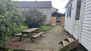 Een grindterras met een houten picknicktafel en banken, omringd door groen en een gebouw met een pannendak.