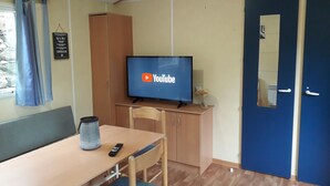 Een kamer met een houten tafel, een televisie waarop het YouTube-logo staat, een kast, een blauwe deur en een raam met gordijnen.