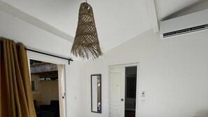 A hotel room with a bed, a hanging light fixture, an air conditioning unit, and a door leading to another room.