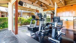 A gym with treadmills and exercise equipment, wooden ceiling beams, and a view of a house.