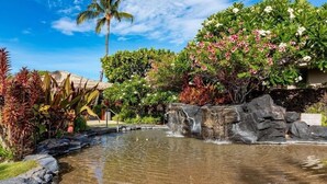 A tropical garden with a pond, palm trees, and various flowering plants.
