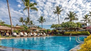 A pool area with lounge chairs and umbrellas, surrounded by palm trees and tropical plants.