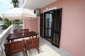 A balcony with a wooden table and chairs, a white umbrella, and a sliding glass door with wooden shutters.