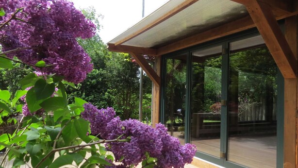 Eine Holzterrasse mit einer Glastür, die zu einem überdachten Außenbereich führt.