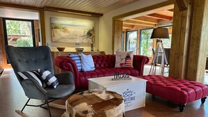 Ein Wohnzimmer mit einem roten Sofa, einem grauen Sessel, einem Schaukelstuhl, einem weißen Couchtisch und einem flauschigen Hocker.