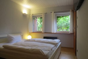 A bedroom with a bed, two windows with curtains, a bedside lamp, and a radiator.