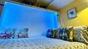 A bedroom with a geometric patterned bedspread, a blue illuminated wall, and a framed picture on the wall. - Shepherds Hut With Hot Tub, North Wales, Anglesey (Llanfairpwllgwyngyll)