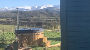 A hot tub in a grassy area with a wooden deck, surrounded by a fence and a shed. - Shepherds Hut With Hot Tub, North Wales, Anglesey (Llanfairpwllgwyngyll)
