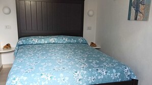 A bedroom with a dark wooden bed frame, a floral bedspread, two bedside tables with lamps, and artwork on the wall. - Residenza l' Ulivo (Parghelia)