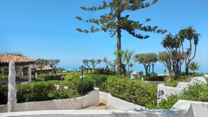 A landscaped garden with a large tree, a pergola, and a view of the sea. - Residenza l' Ulivo (Parghelia)