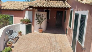A courtyard with a tiled floor, potted plants, a bench, and a door leading to a building with green shutters. - Residenza l' Ulivo (Parghelia)