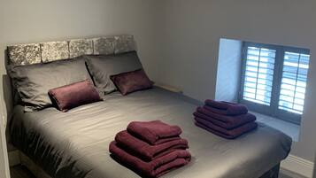 A modern bedroom with a large bed, a headboard with a distressed finish, and a window with blinds.