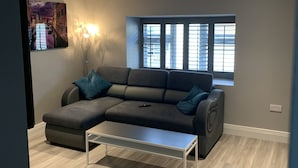 Een moderne woonkamer met een hoekbank, een salontafel en een groot raam met zonwering.
