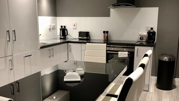 Een moderne keuken met een centraal eiland, inbouwapparatuur en een eethoek met stoelen.