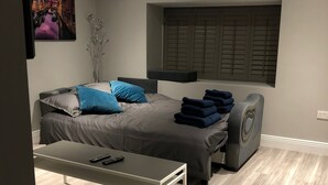 Een moderne slaapkamer met een bed, nachtkastjes, een bankje en een raam met luiken.