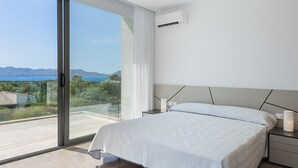 A modern bedroom with a large sliding glass door leading to a balcony with a scenic view of the sea and mountains. - Luxurious Villa Amer with Private Pool in Bonaire Alcúdia (Alcúdia)