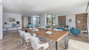 A modern dining area with a wooden table, white chairs, and a glass partition. - Luxurious Villa Amer with Private Pool in Bonaire Alcúdia (Alcúdia)