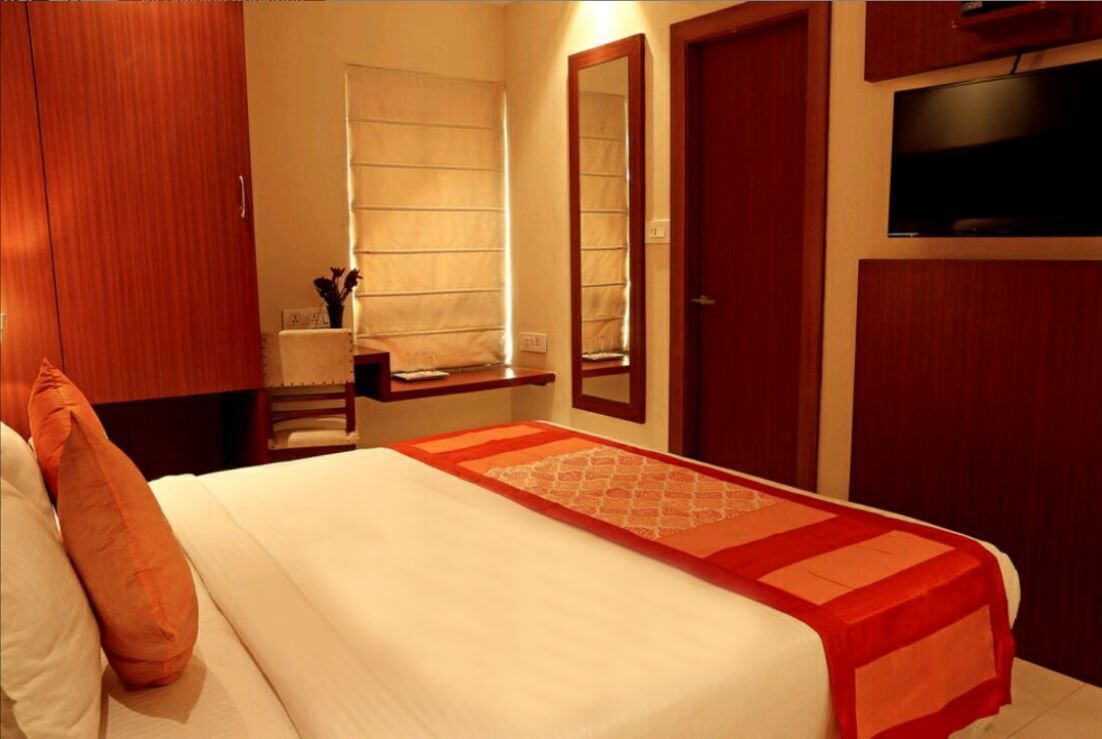 A hotel room with a bed, a TV mounted on the wall, and a wooden wardrobe.