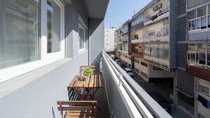 Un balcón con mesa y sillas, con vista a una calle con coches aparcados y edificios.