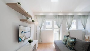 Una sala moderna con un sofá, un televisor de pantalla plana, estanterías de madera y una ventana con cortinas.