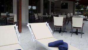 A covered outdoor seating area with lounge chairs and tables, large windows, and a view of the surrounding greenery. - Hotel Fortuna B&B (Costermano sul Garda)