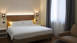 A hotel room with a large bed, two bedside tables, a chair, and a window with curtains. - Hotel Fortuna B&B (Costermano sul Garda)