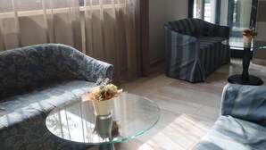 A modern living room with a sofa, a glass coffee table with a vase of flowers, and a striped armchair. - Hotel Fortuna B&B (Costermano sul Garda)
